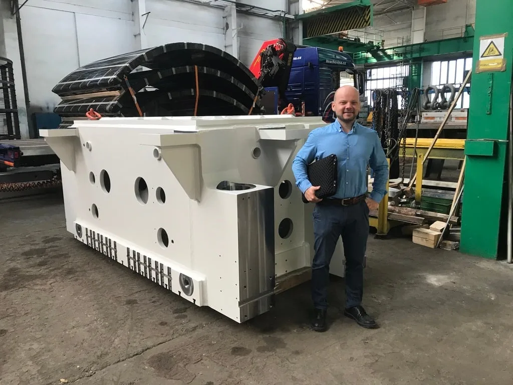 Gabriel Haulik standing beside a large manufactured machine structure in a factory